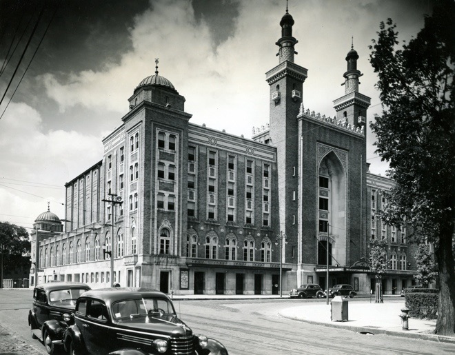 Historic building with distinctive architecture, featuring towers and ornate details, surrounded by vintage cars on a street.