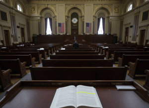 Documentary-style wide shot of an almost entirely empty House chamber. The chamber is grand — high ceilings, tiered seating, American flags — but nearly every seat is vacant. A single figure stands at the lectern at the front. A large clock on the wall reads 10:34. On the desk in the foreground sits an open Congressional Record, with a section highlighted titled "Executive Communications." The mood is one of institutional theater — an enormous room, four minutes of business, and a stack of consequential documents nobody is reading aloud. Dry, bureaucratic, slightly absurd.